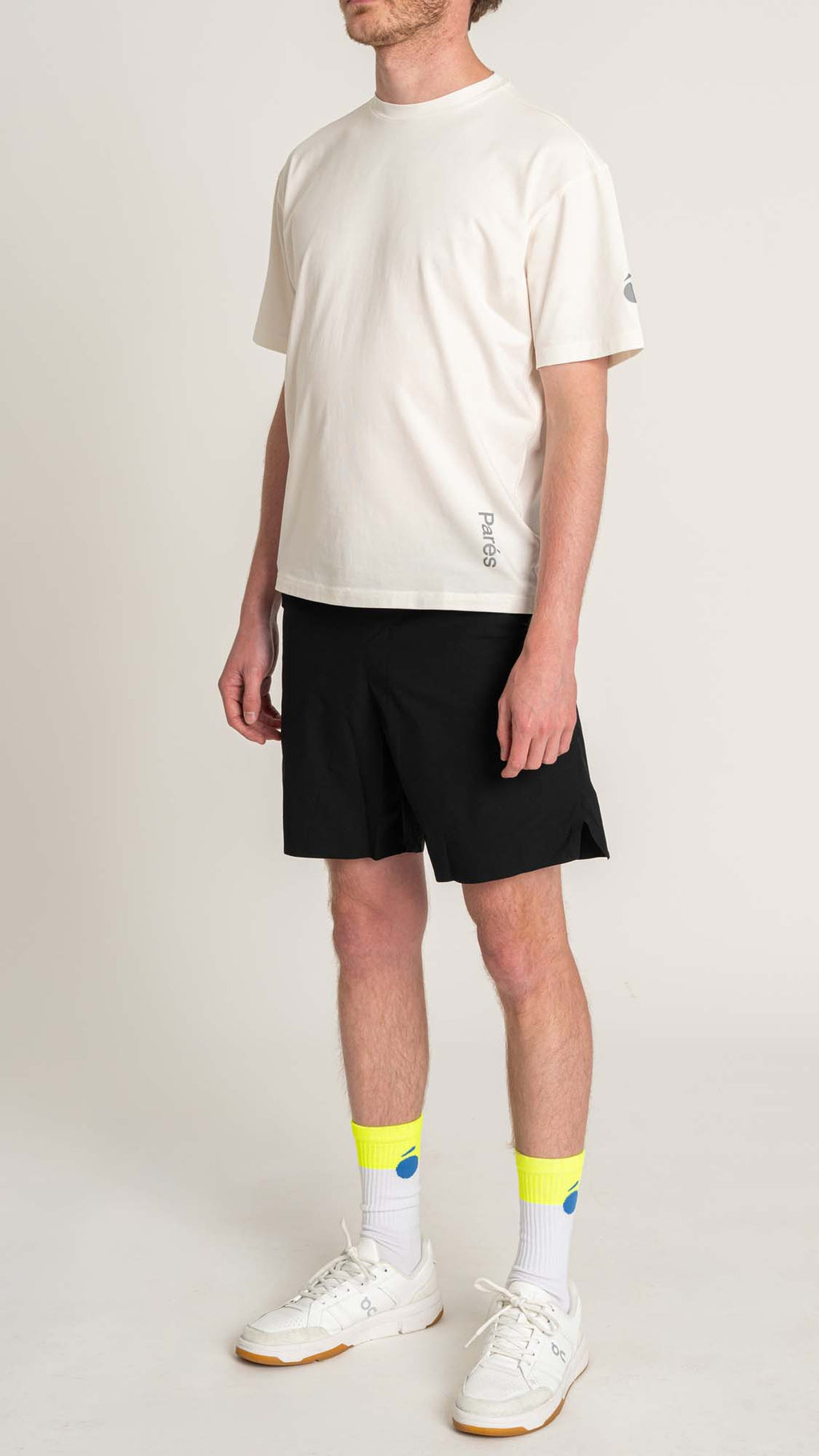 Person wearing a white t-shirt, black shorts, and white sneakers with yellow socks on a plain background